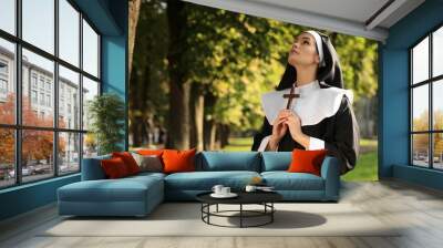 Young nun with Christian cross in park on sunny day, space for text Wall mural