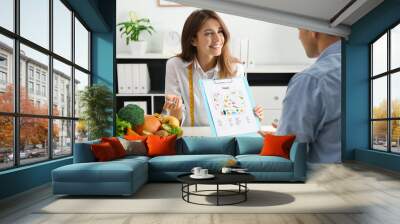 Young nutritionist consulting patient at table in clinic Wall mural