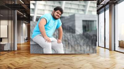 Young overweight man in sportswear resting outdoors Wall mural