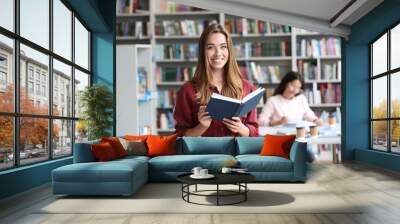 Young pretty woman with book in library Wall mural