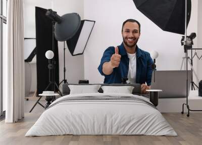 Young professional photographer with camera showing thumbs up in modern photo studio Wall mural