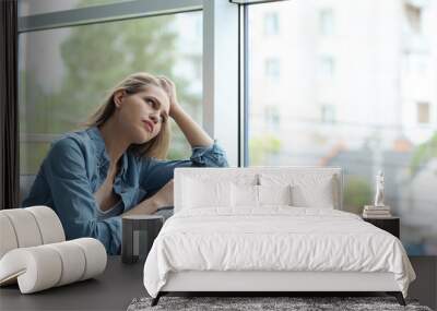 Young sad woman sitting near window at home Wall mural