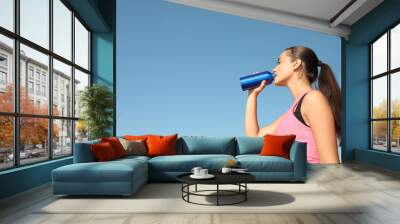 Young sporty woman drinking from water bottle outdoors on sunny day. Space for text Wall mural