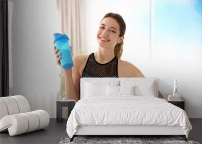 Young sporty woman with bottle of protein shake at home Wall mural