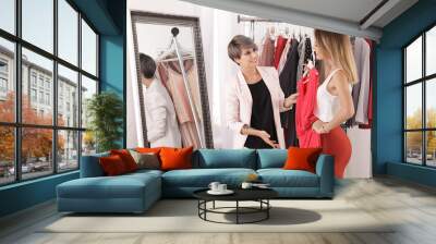 Young stylist helping client to choose trendy clothes in studio Wall mural