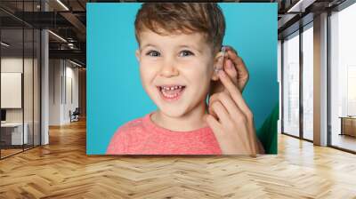 Young woman adjusting little son's hearing aid on color background, closeup Wall mural