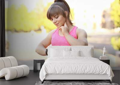 Young woman checking pulse after workout in park Wall mural