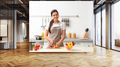 Young woman cutting vegetables for soup at table in kitchen Wall mural