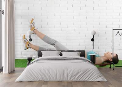 Young woman doing scissors exercise on carpet near brick wall. Space for text Wall mural