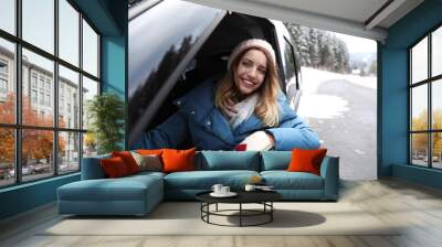 Young woman driving car and looking out of window on road. Winter vacation Wall mural