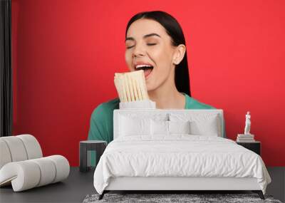 Young woman eating delicious shawarma on red background Wall mural