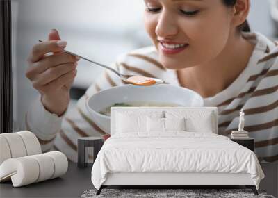 Young woman eating tasty vegetable soup indoors Wall mural