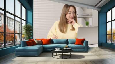 Young woman having video chat via laptop at white table indoors Wall mural