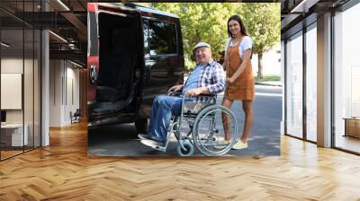 Young woman helping senior man in wheelchair to get into van outdoors Wall mural