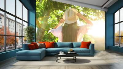 Young woman in hat outdoors on sunny day, back view Wall mural