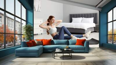 Young woman in sportswear doing exercises on fitness mat in bedroom Wall mural