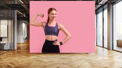 Young woman in sportswear showing muscles on pink background, space for text Wall mural