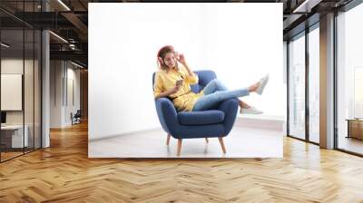 Young woman listening to music in armchair at home. Space for text Wall mural