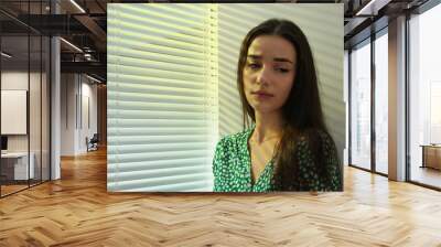 Young woman near window with Venetian blinds. Space for text Wall mural