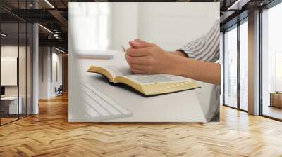 Young woman praying over Bible at desk, closeup Wall mural