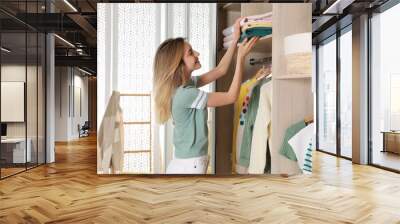 Young woman putting clothes into wardrobe at home Wall mural