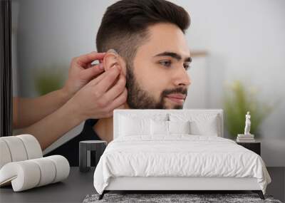 Young woman putting hearing aid in man's ear indoors Wall mural