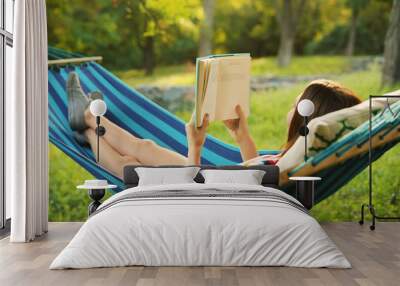 Young woman reading book in comfortable hammock at green garden Wall mural