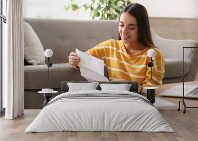 Young woman reading paper letter at home Wall mural