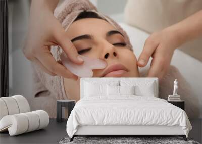 Young woman receiving facial massage with gua sha tool in beauty salon Wall mural