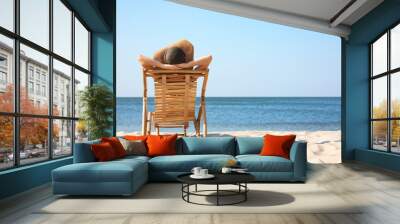 Young woman relaxing in deck chair on sandy beach Wall mural