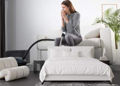 Young woman suffering from dust allergy while vacuuming house Wall mural