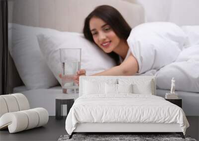 Young woman taking glass of water from nightstand at home, focus on hand Wall mural