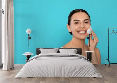 Young woman using cotton pad with micellar water on light blue background, space for text Wall mural