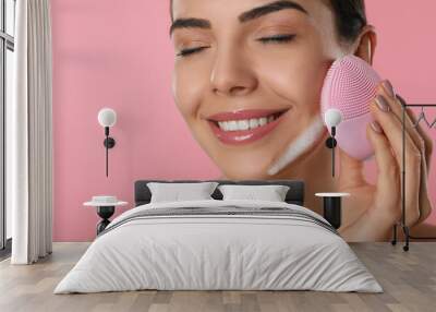 Young woman using facial cleansing brush on pink background, closeup. Washing accessory Wall mural