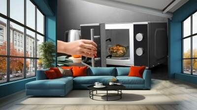 Young woman using microwave oven on table in kitchen Wall mural