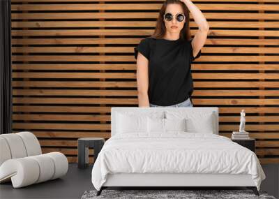 Young woman wearing black t-shirt against wooden wall on street. Urban style Wall mural