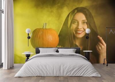 Young woman wearing witch costume with pumpkin in smoke cloud on dark background. Halloween party Wall mural