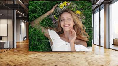 Young woman wearing wreath made of beautiful flowers on green grass, top view Wall mural