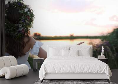 Young woman wearing wreath made of beautiful flowers outdoors at sunset, back view Wall mural