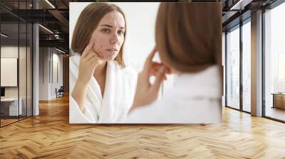 Young woman with acne problem near mirror in bathroom Wall mural