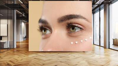 Young woman with cream around eye on beige background, closeup Wall mural