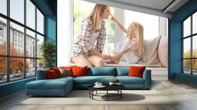 Young woman with cute little girl near window at home Wall mural