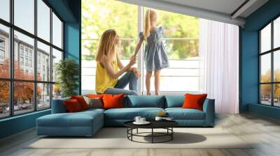 Young woman with cute little girl near window at home Wall mural