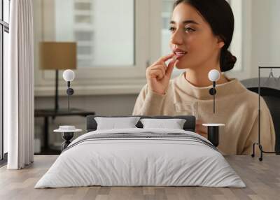 Young woman with glass of water taking dietary supplement pill indoors, space for text Wall mural