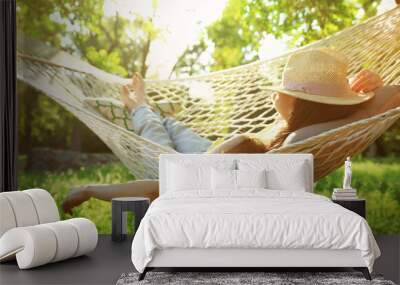 Young woman with hat resting in comfortable hammock at green garden Wall mural