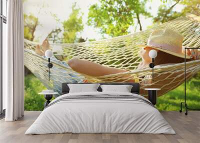 Young woman with hat resting in comfortable hammock at green garden Wall mural