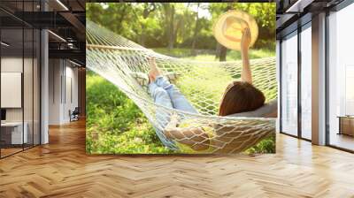 Young woman with hat resting in comfortable hammock at green garden Wall mural