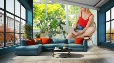 Young woman with laptop sitting in armchair at indoor terrace Wall mural