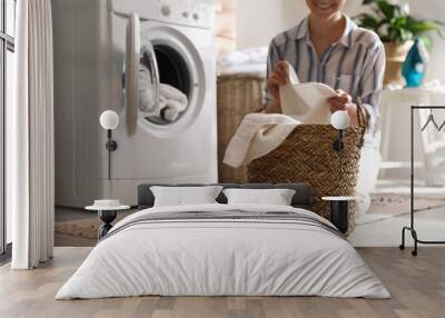 Young woman with laundry basket near washing machine at home Wall mural