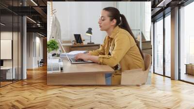 Young woman with poor posture using laptop at table indoors Wall mural